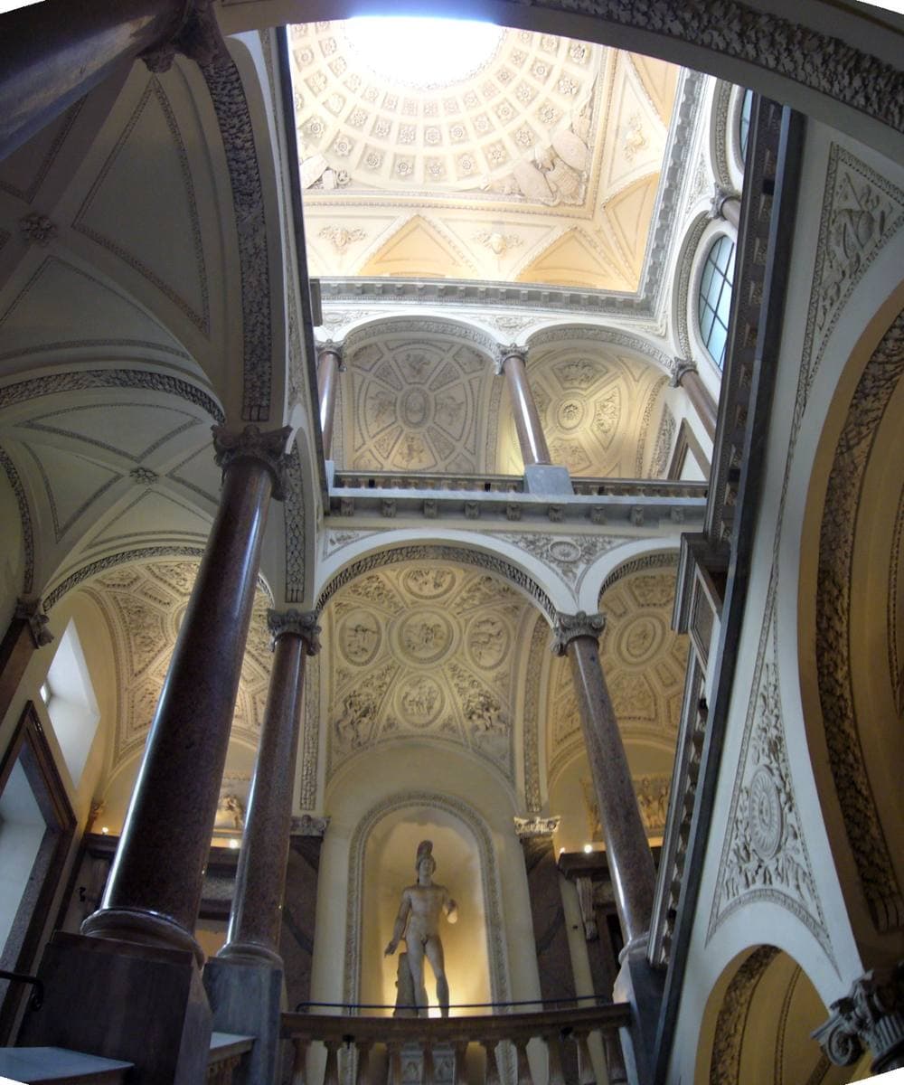 Looking up a white and gold staircase hall to a domed ceiling