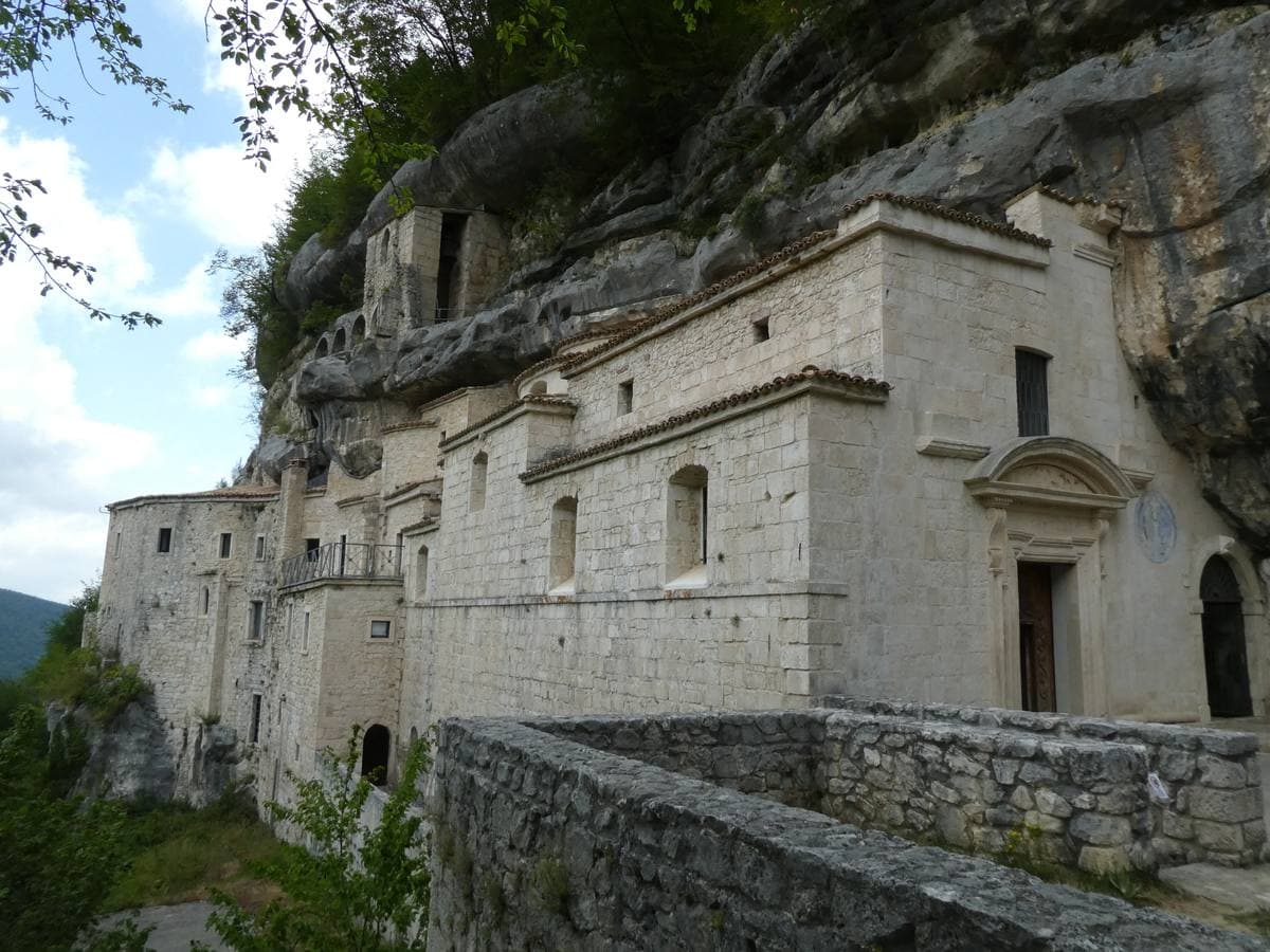 Stone hermitage buildings set against an overhanging limestone cliff