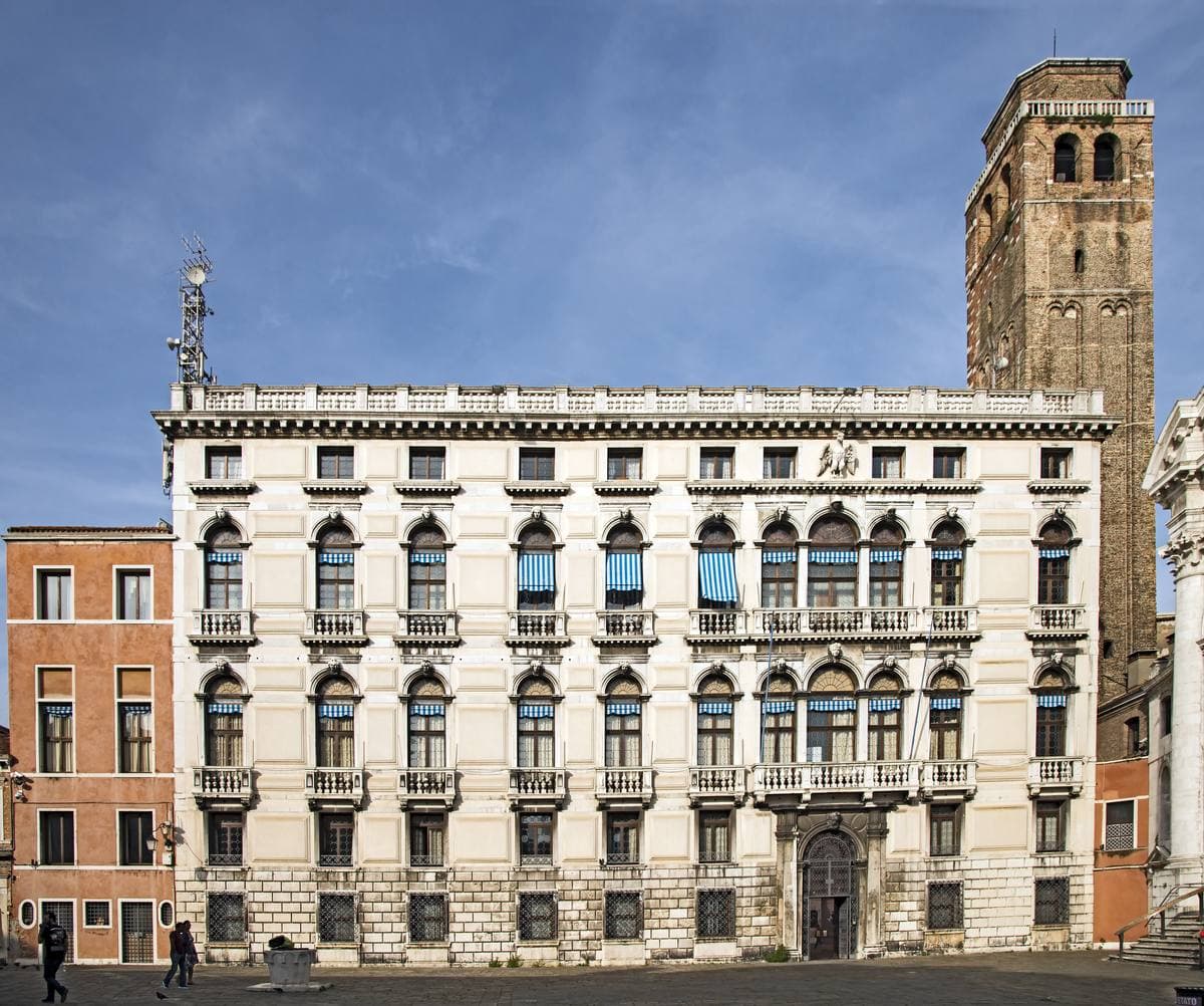 A pale stone Venetian palace front with a tall brick bell tower beside it