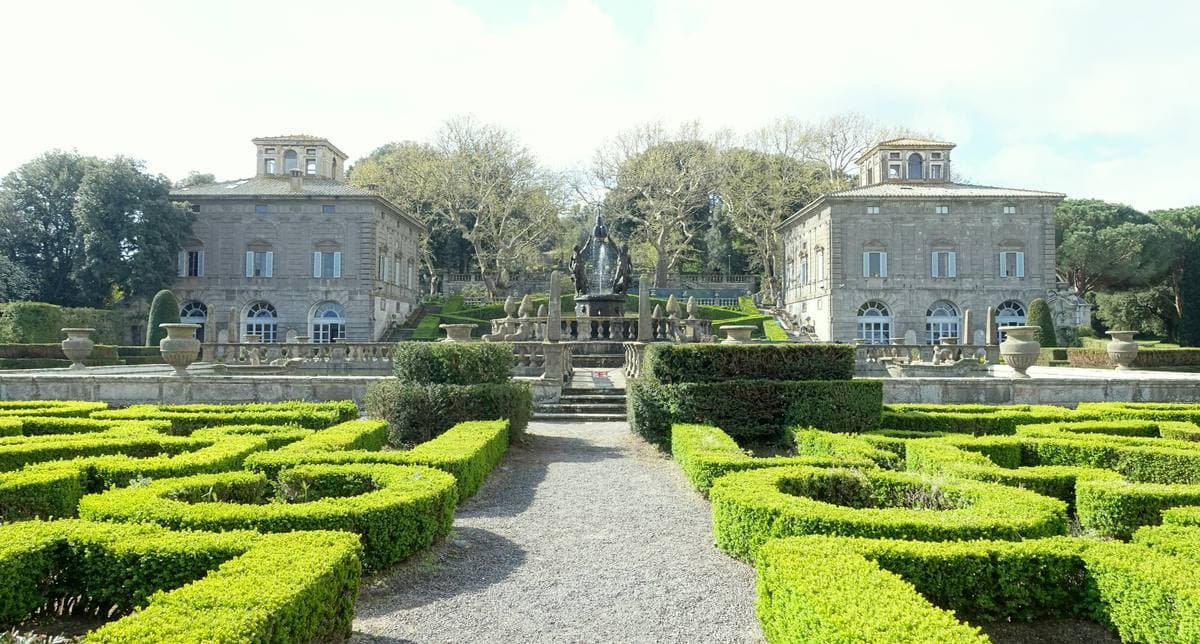 Two matching villas behind a garden of clipped box hedges around a fountain