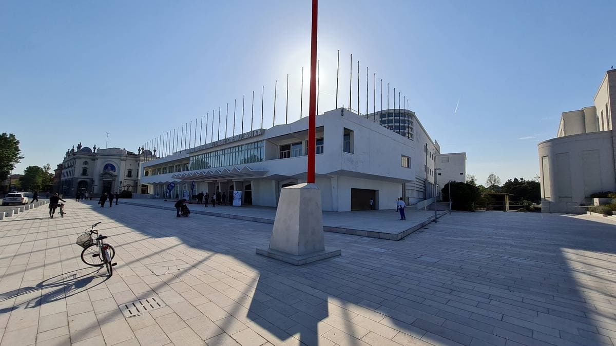 A white modernist festival building on a wide paved square under a bright sky