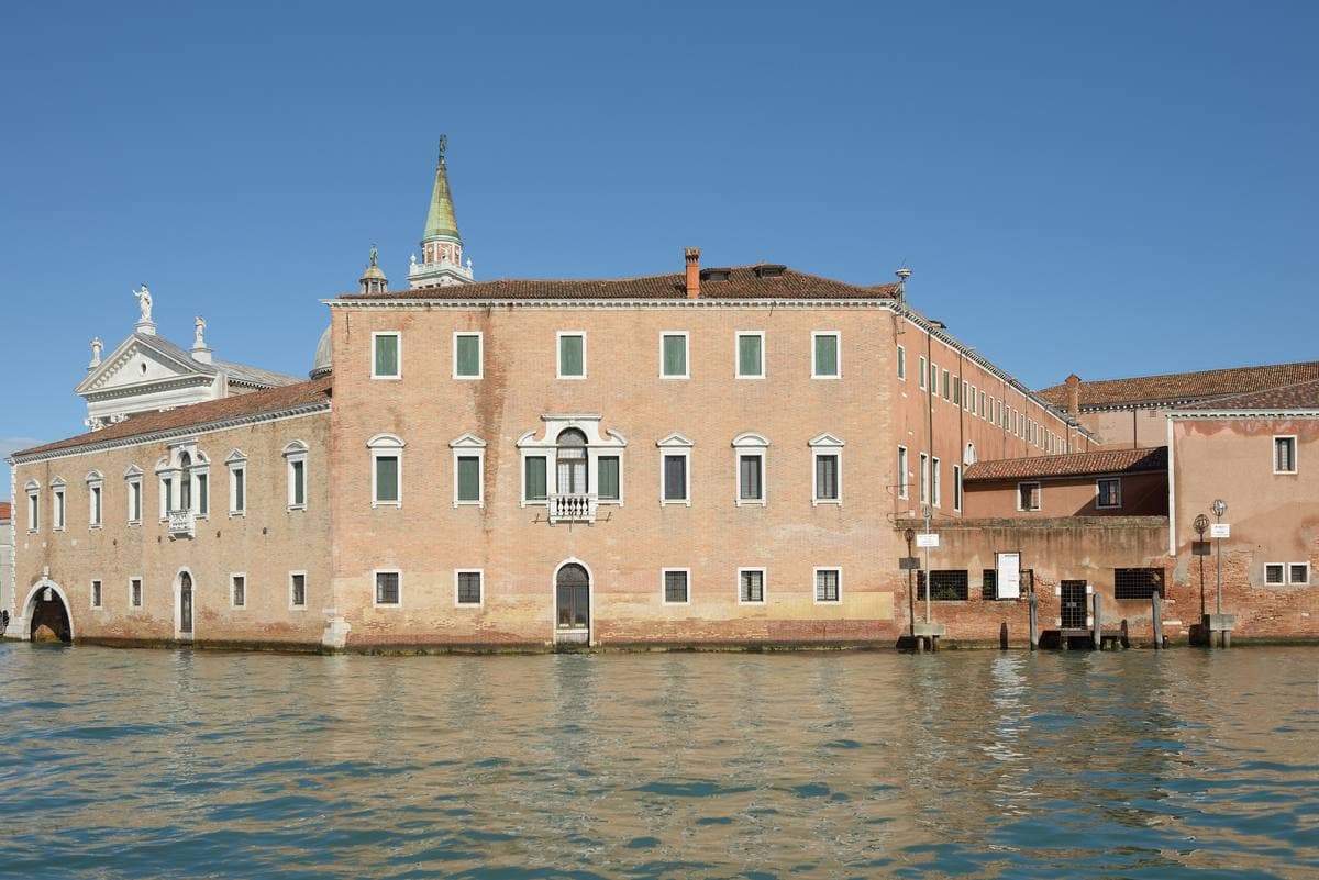 A long pink monastery front on the water, a bell tower behind