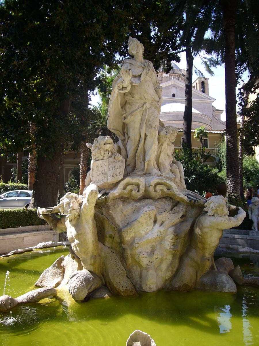 A white marble fountain group rising from a green pool among palms