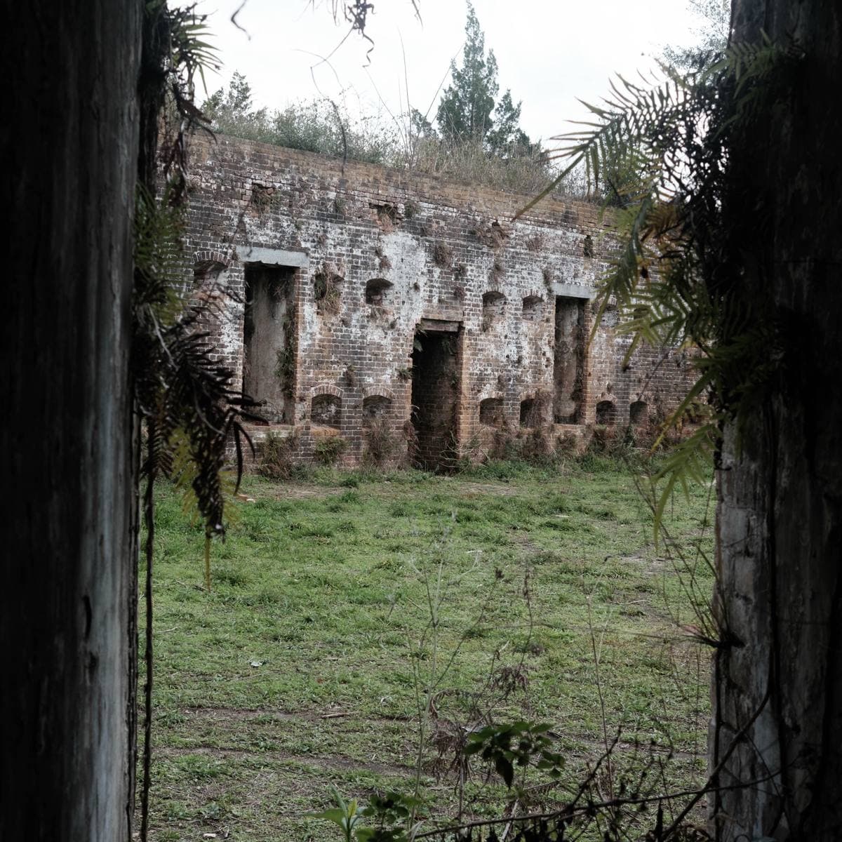 Brick casemates of a ruined fort seen through a dark archway, grass in the yard