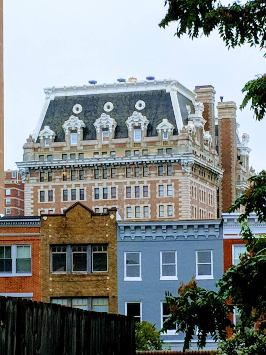 An ornate mansard-roofed tower block rising behind a row of painted brick houses