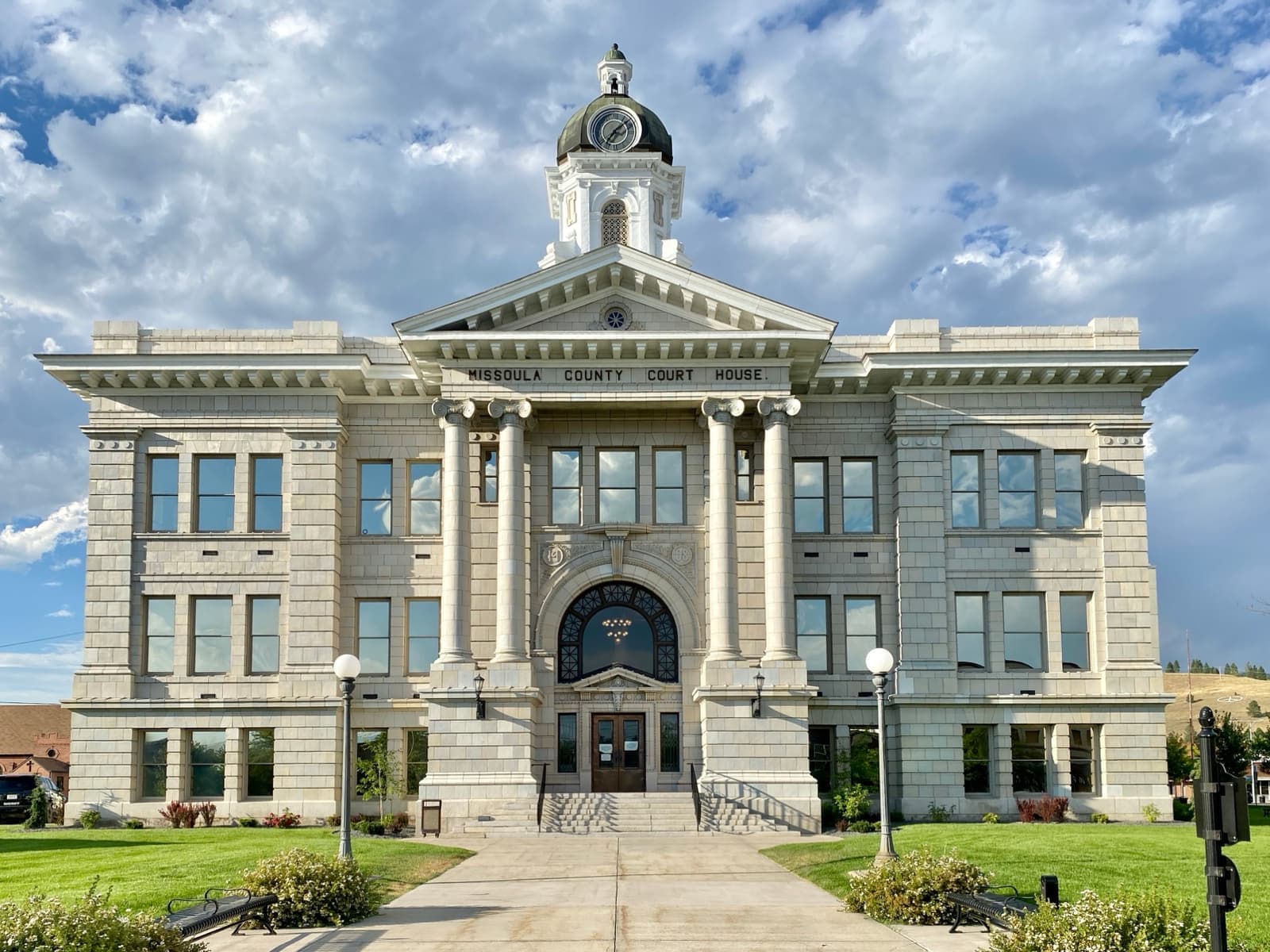 A pale stone courthouse with columns and a clock cupola behind a lawn and path