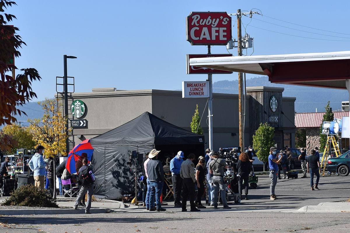 A film crew, tents and trucks in a diner car park on Reserve Street, Missoula, with mountains behind