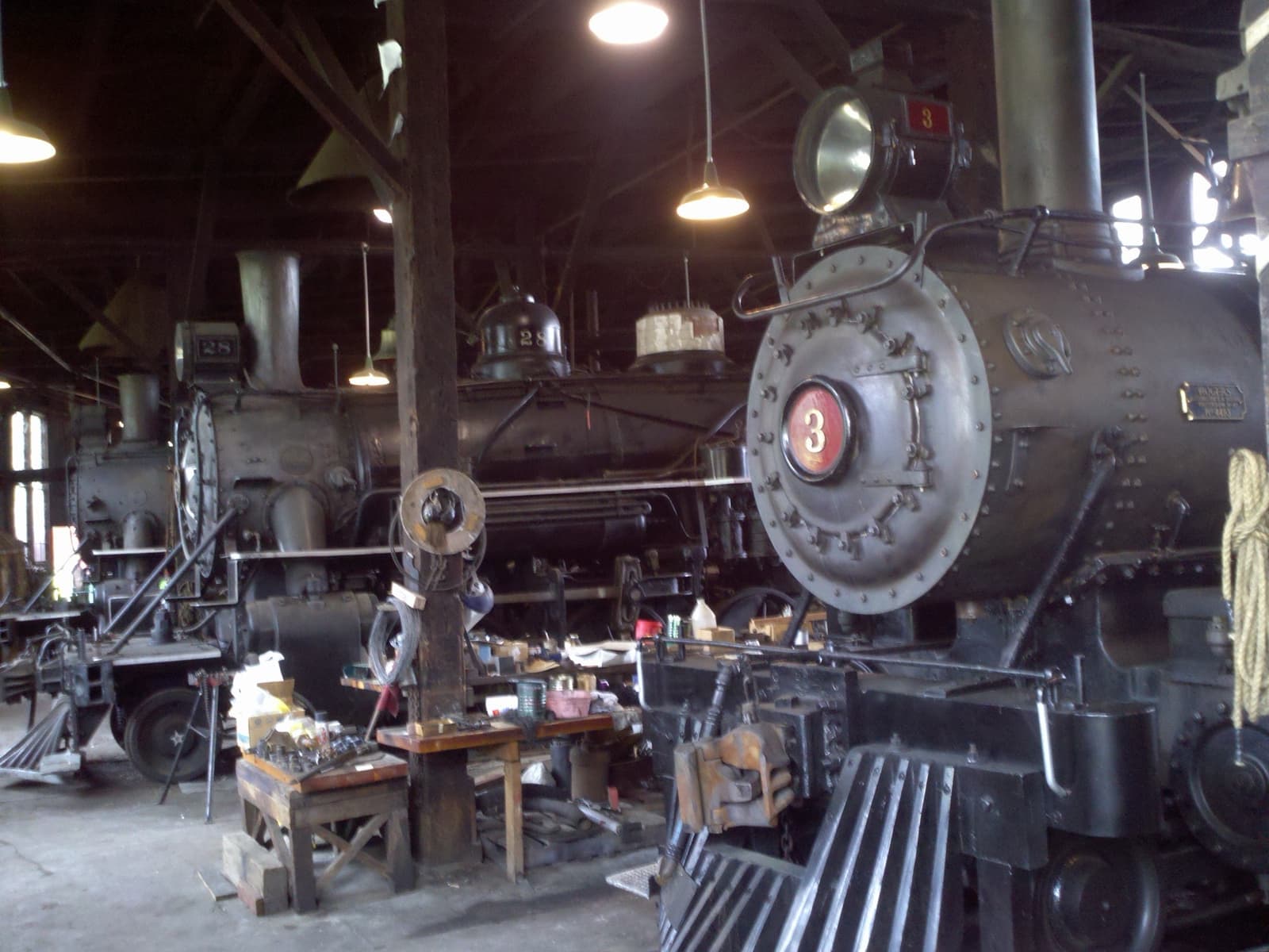 A black steam locomotive with a red number 3 on its smokebox, inside a timber roundhouse
