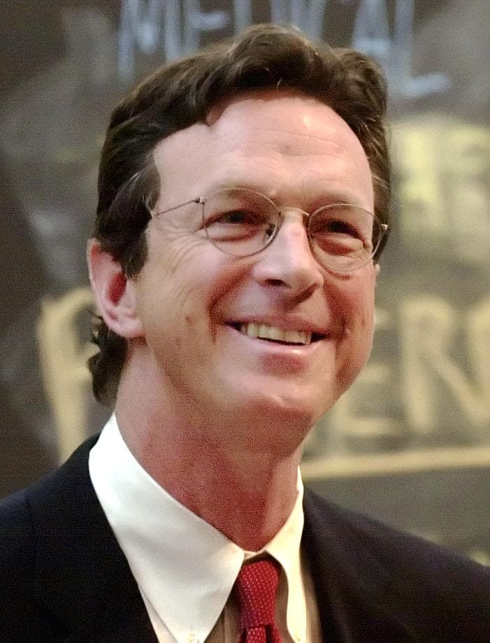 Michael Crichton smiling, in glasses and a dark suit