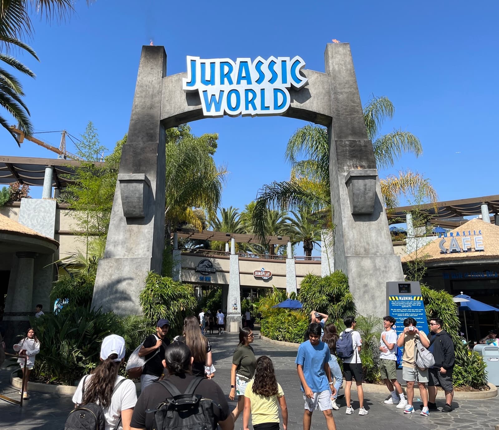 Visitors walking under a tall stone-effect gateway into a jungle-themed ride