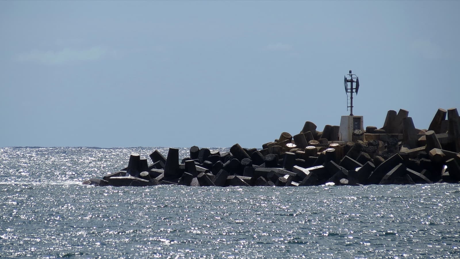 A rock breakwater with a small light tower in a grey-blue bay