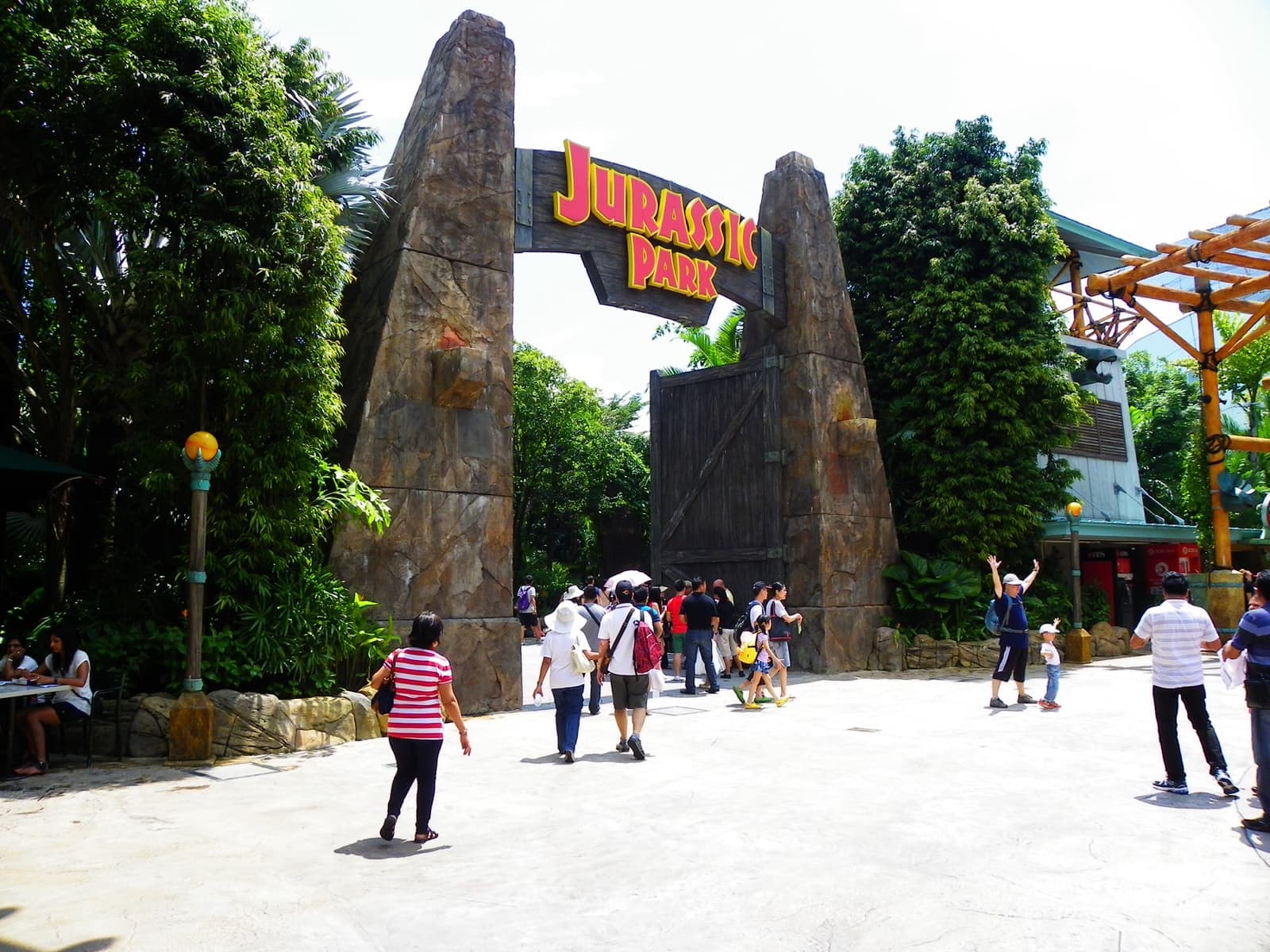 Visitors passing through a large gate flanked by stone pillars and palms