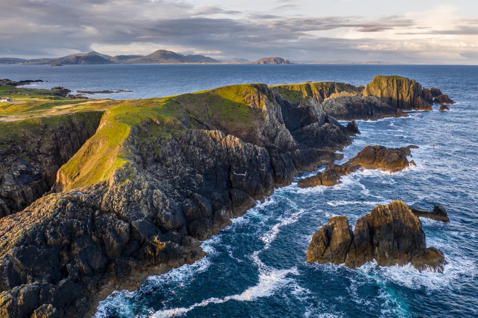 Green headland and rocky shore under a wide sky at the tip of Ireland