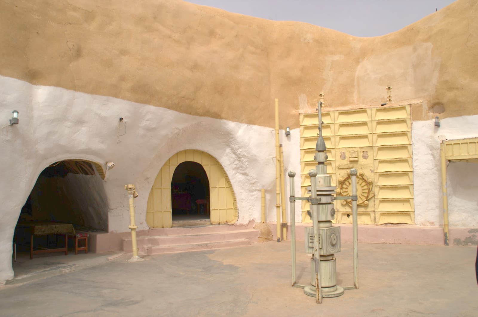 A round sunken courtyard cut into pale earth, with whitewashed doorways and steps