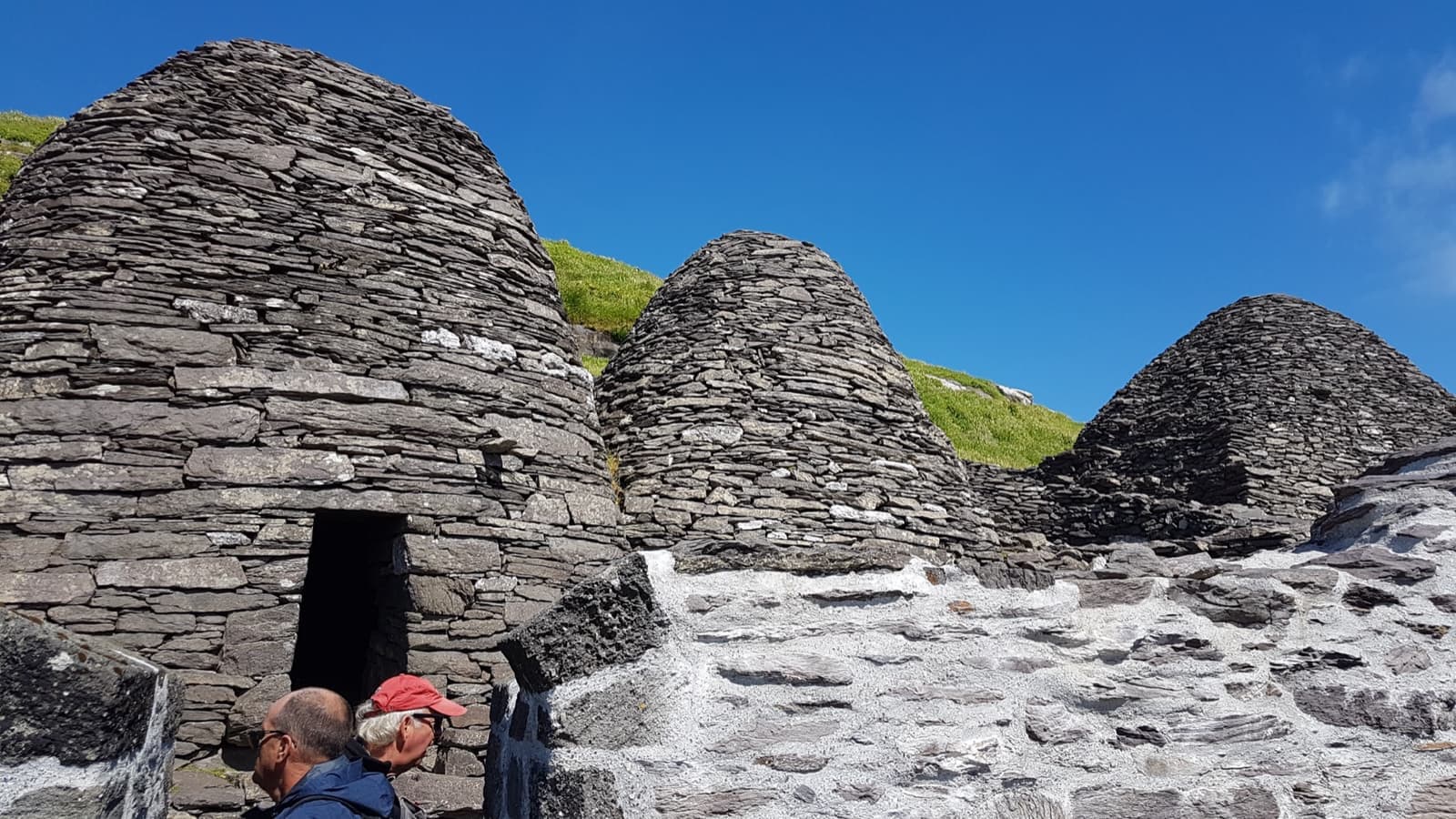 Dry-stone beehive-shaped huts on a grassy terrace high above the sea