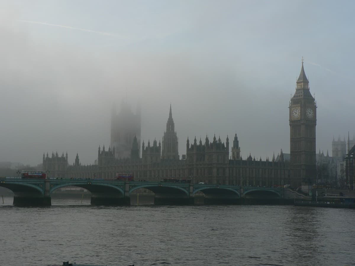 Red buses crossing a bridge towards a Gothic palace and clock tower