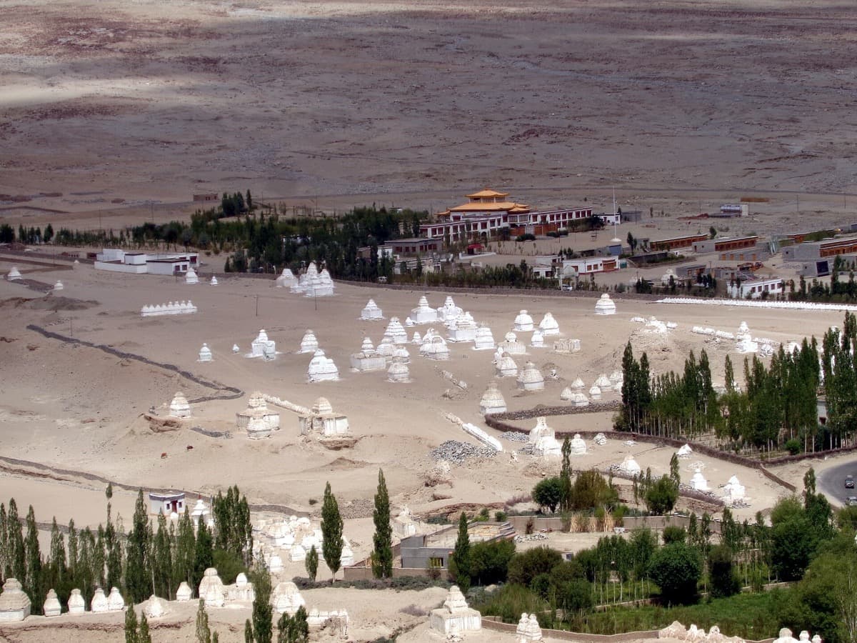 A white school building and a hillside monastery under a clear Ladakh sky