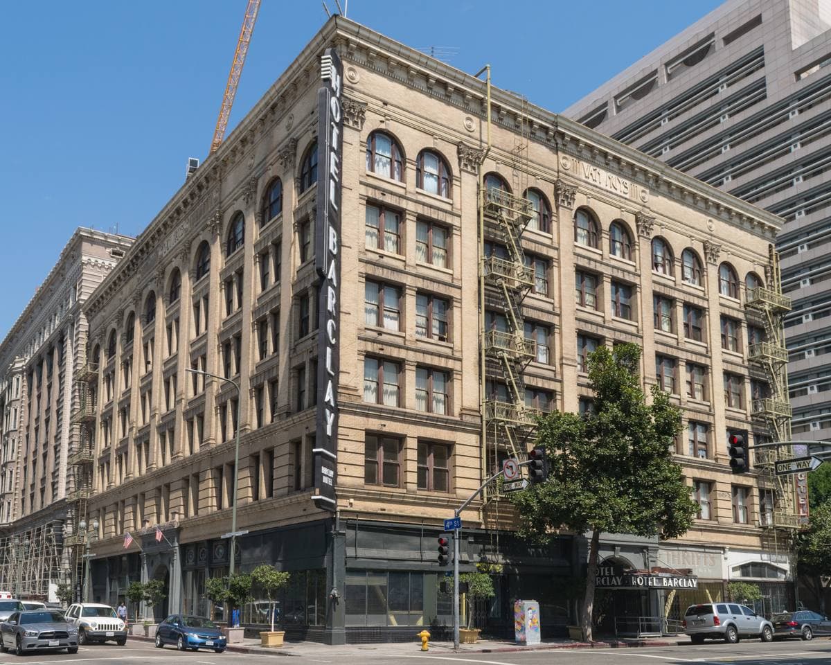 A pale six-storey Beaux-Arts hotel building on a street corner with trees in front
