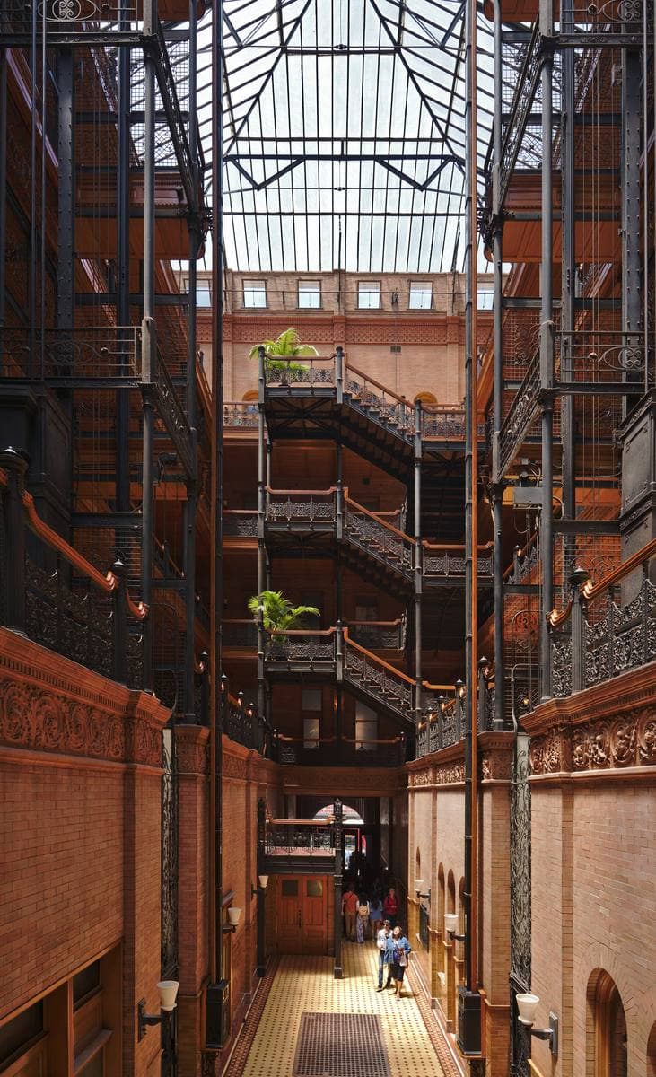 A tall light court with iron stairways, railings and open lift cages under a glass roof