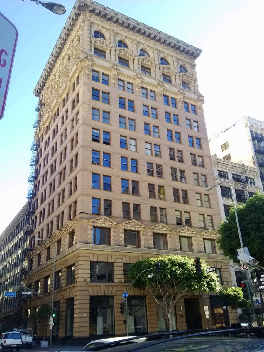 A tall, narrow cream office building with a heavy cornice, seen from the street below