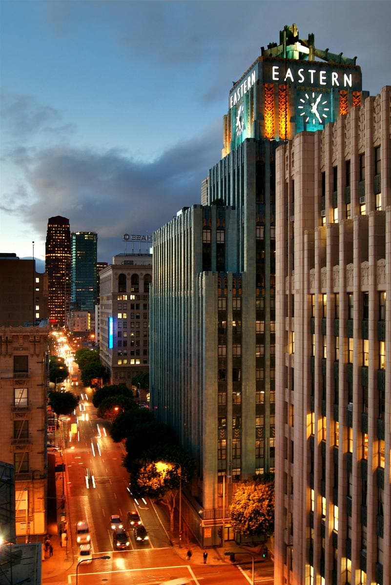 A turquoise Art Deco tower with a clock and the word EASTERN at the top, above a lit street at dusk