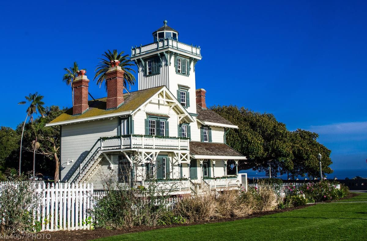 A white wooden Victorian lighthouse with a lantern tower and red chimneys under a deep blue sky