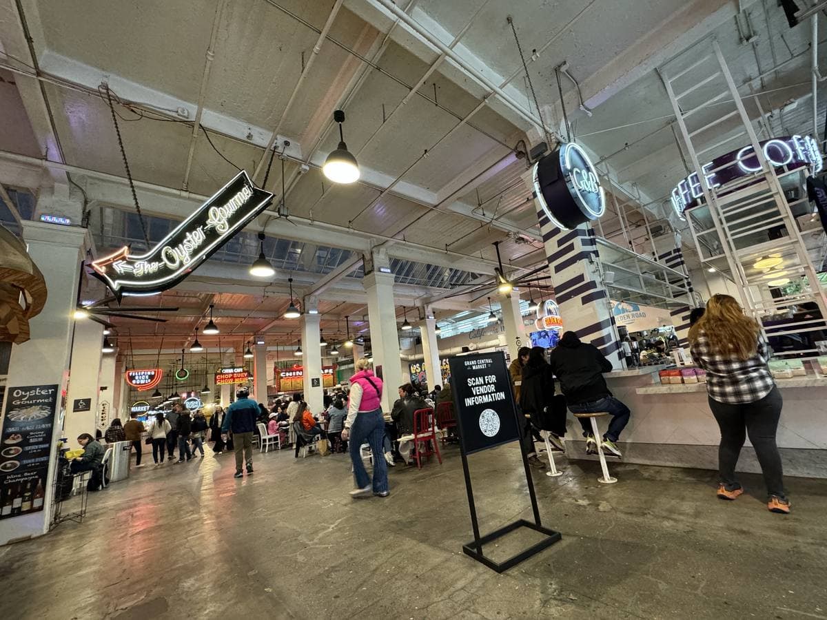 A busy market hall with neon signs, counters and people walking down the aisle