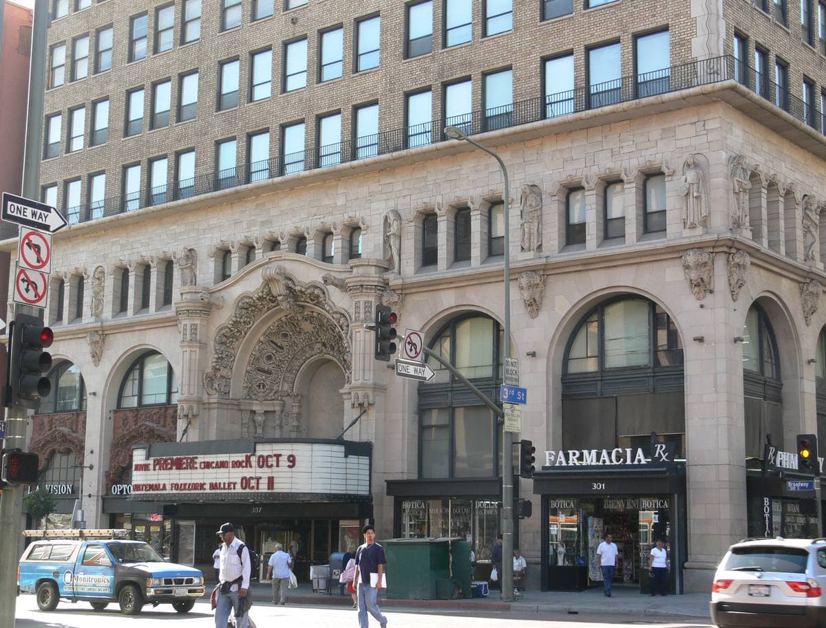 An ornate pale stone theatre front with a marquee on a downtown street corner