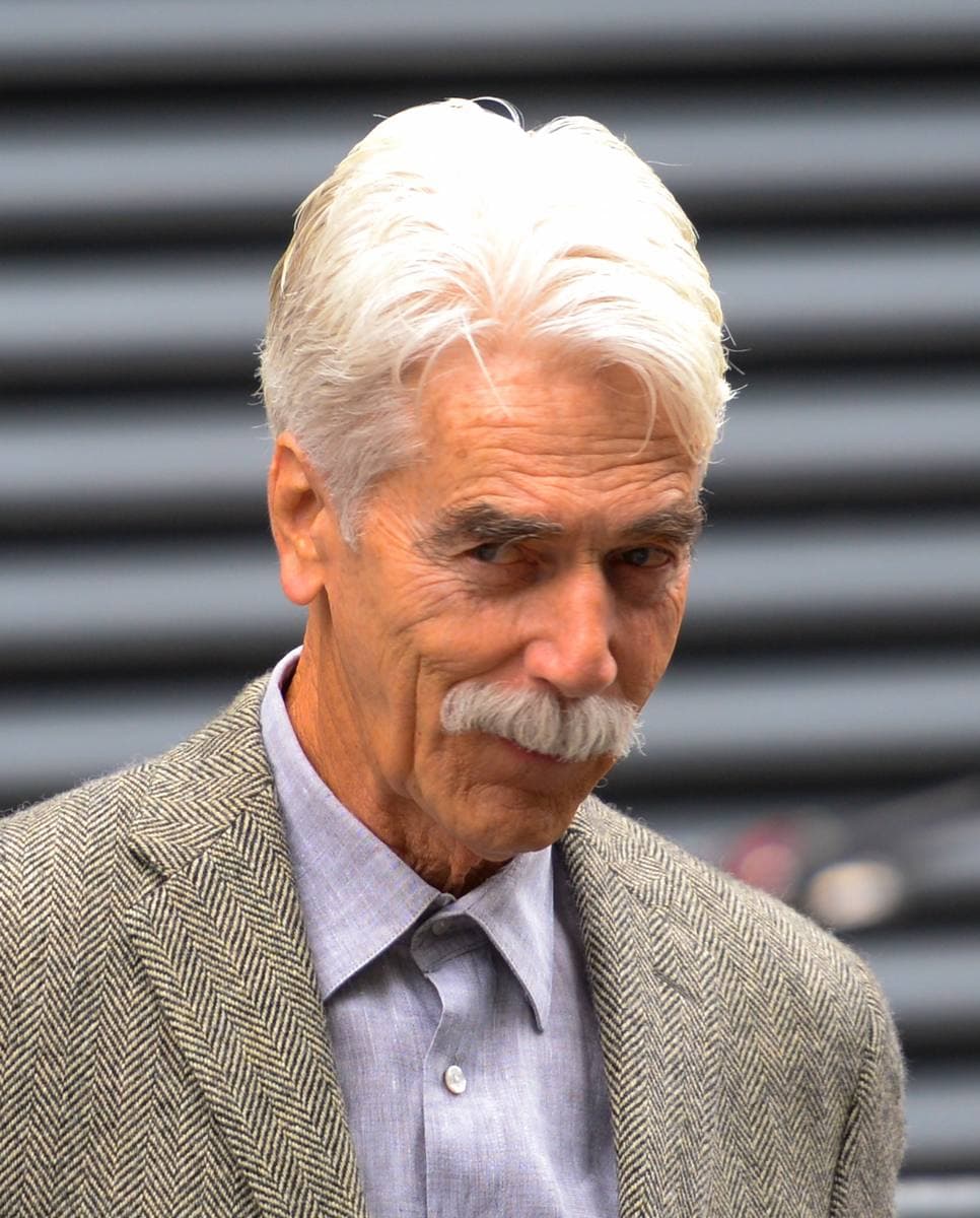 Sam Elliott, white hair and a white moustache, in a grey jacket