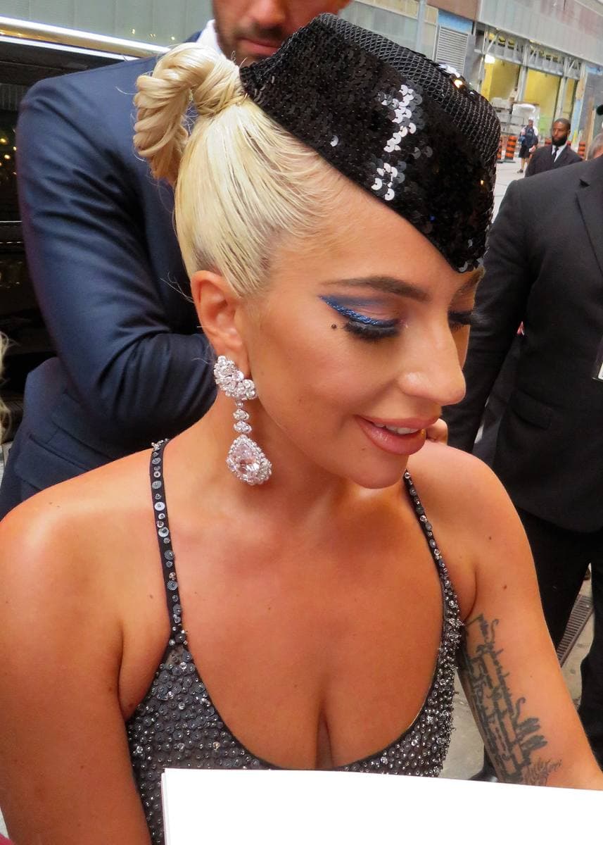 Lady Gaga with platinum hair under a small black sequinned hat, smiling down