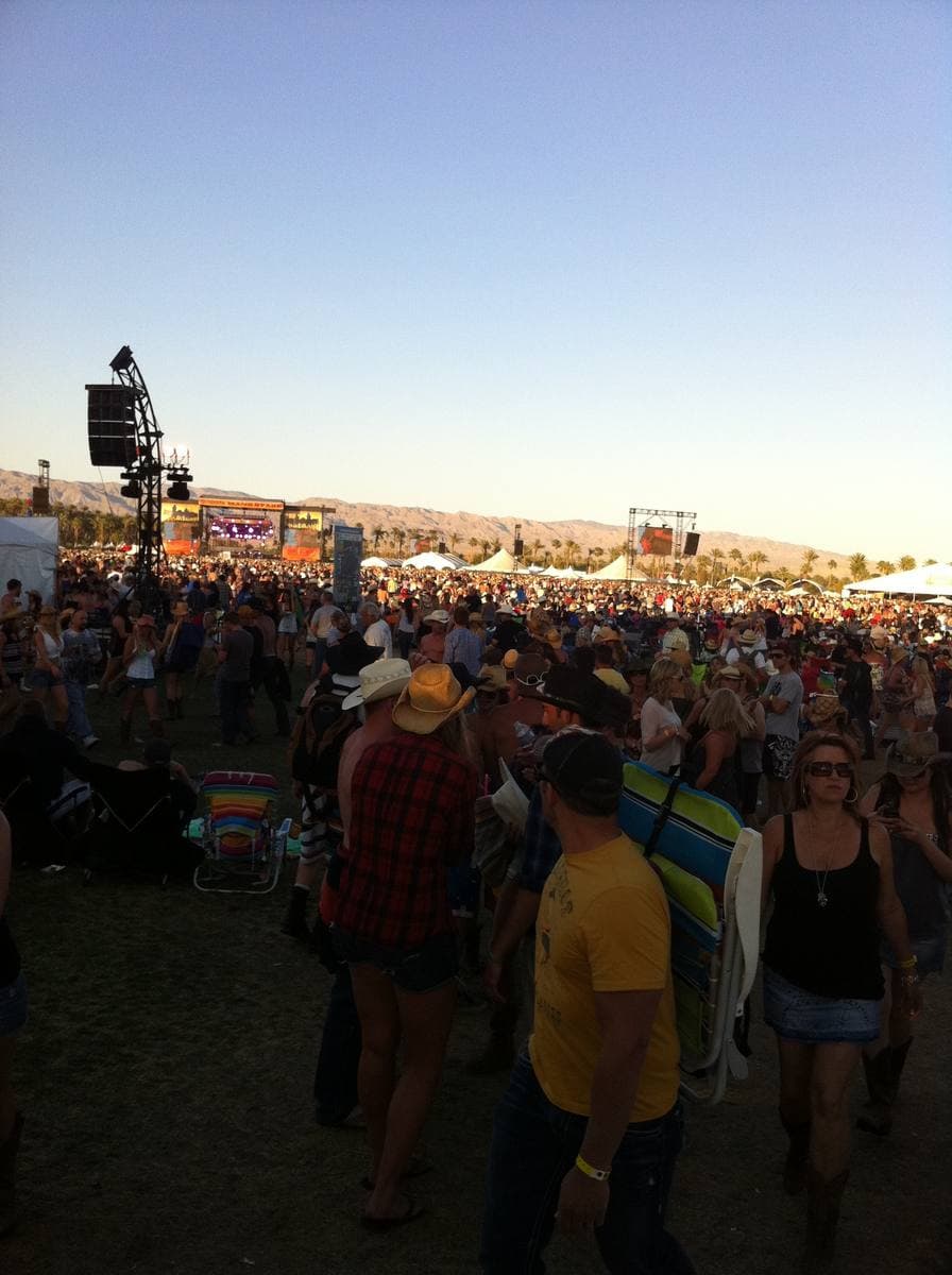 A crowd in cowboy hats in front of a distant festival stage at dusk