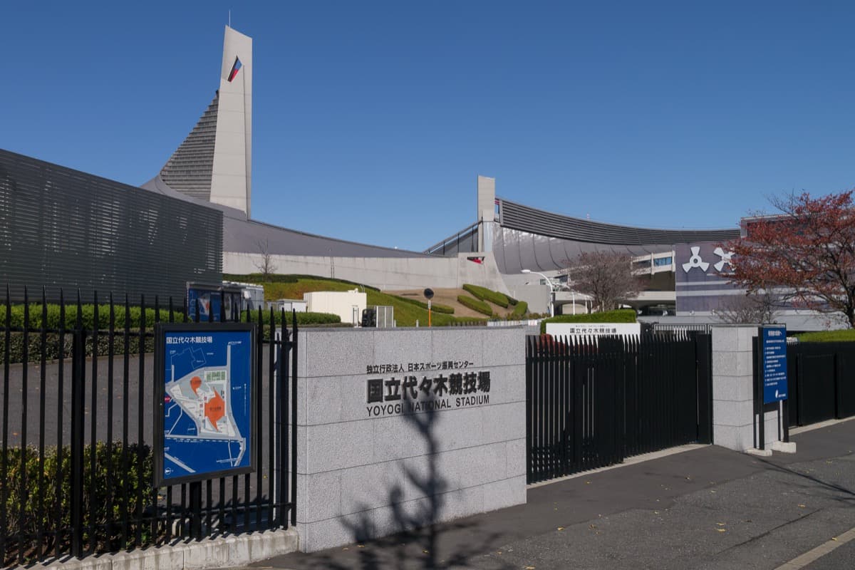 The tower and curved roofs of Yoyogi National Gymnasium behind a gate and an entrance sign