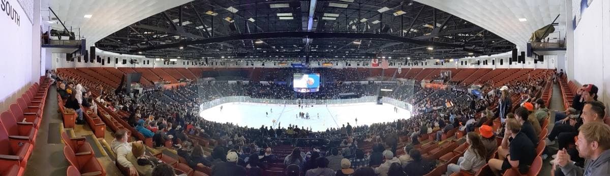 A wide panorama of an arena bowl with red seats around an ice rink
