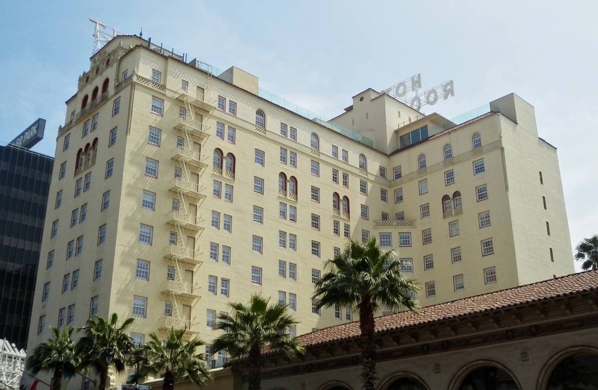 A cream Spanish Colonial hotel with a red-tiled roof and palm trees in front