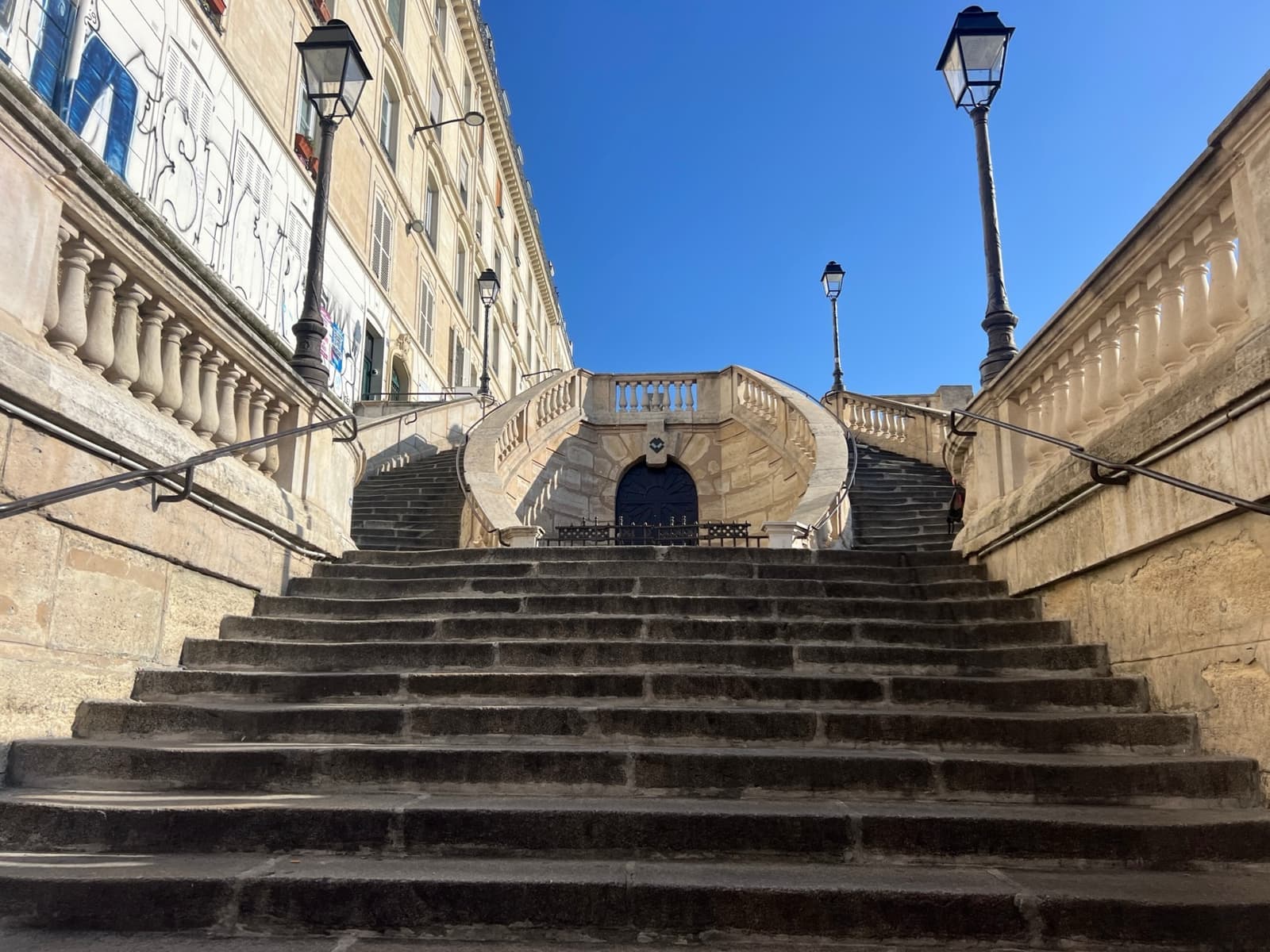 A broad stone stairway rising to a curved double flight under a blue sky
