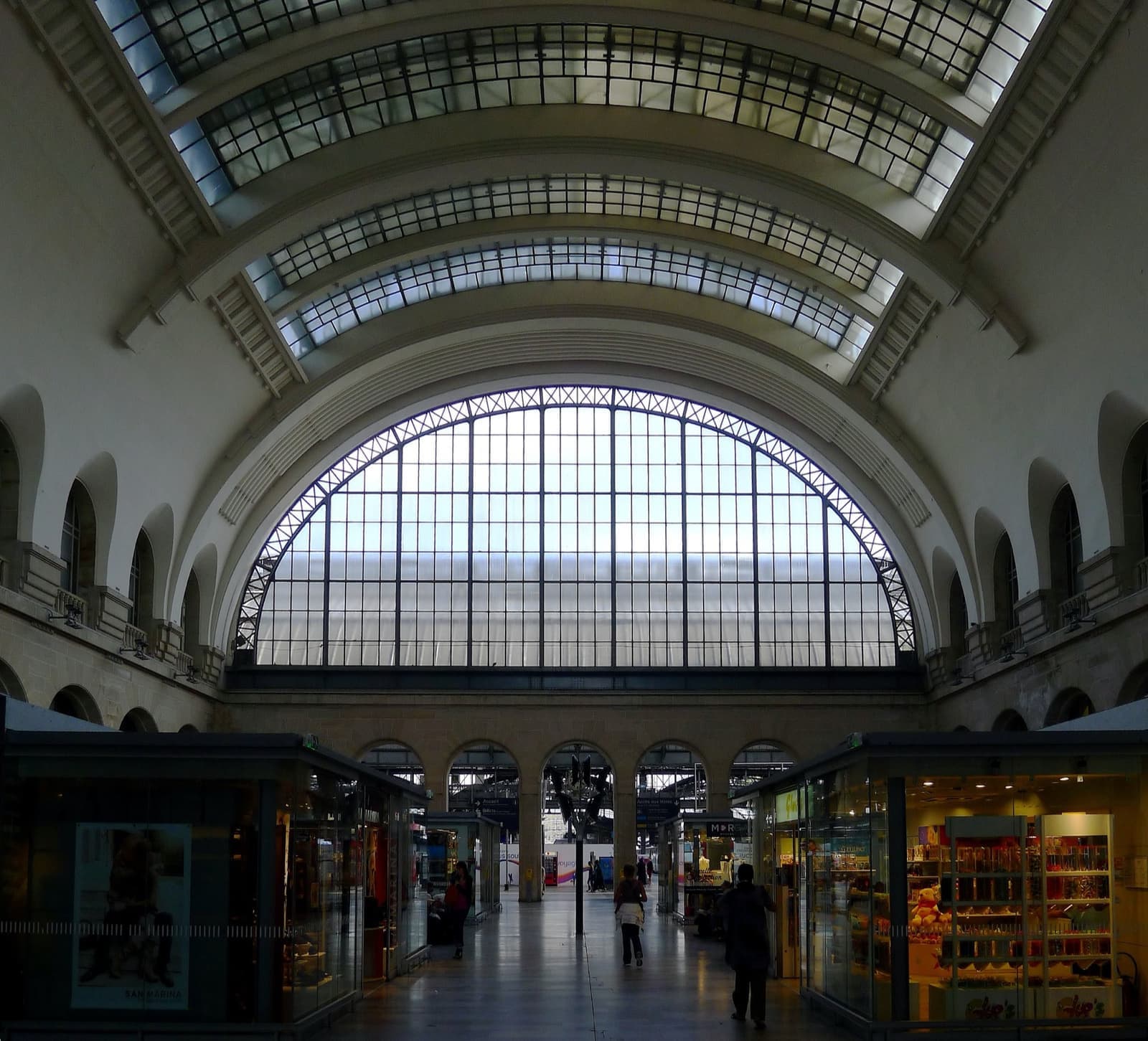 A vaulted station hall with a half-moon window and shopfronts along both sides