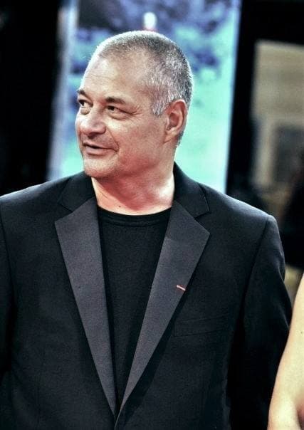 Jean-Pierre Jeunet in a black jacket and T-shirt, smiling to one side