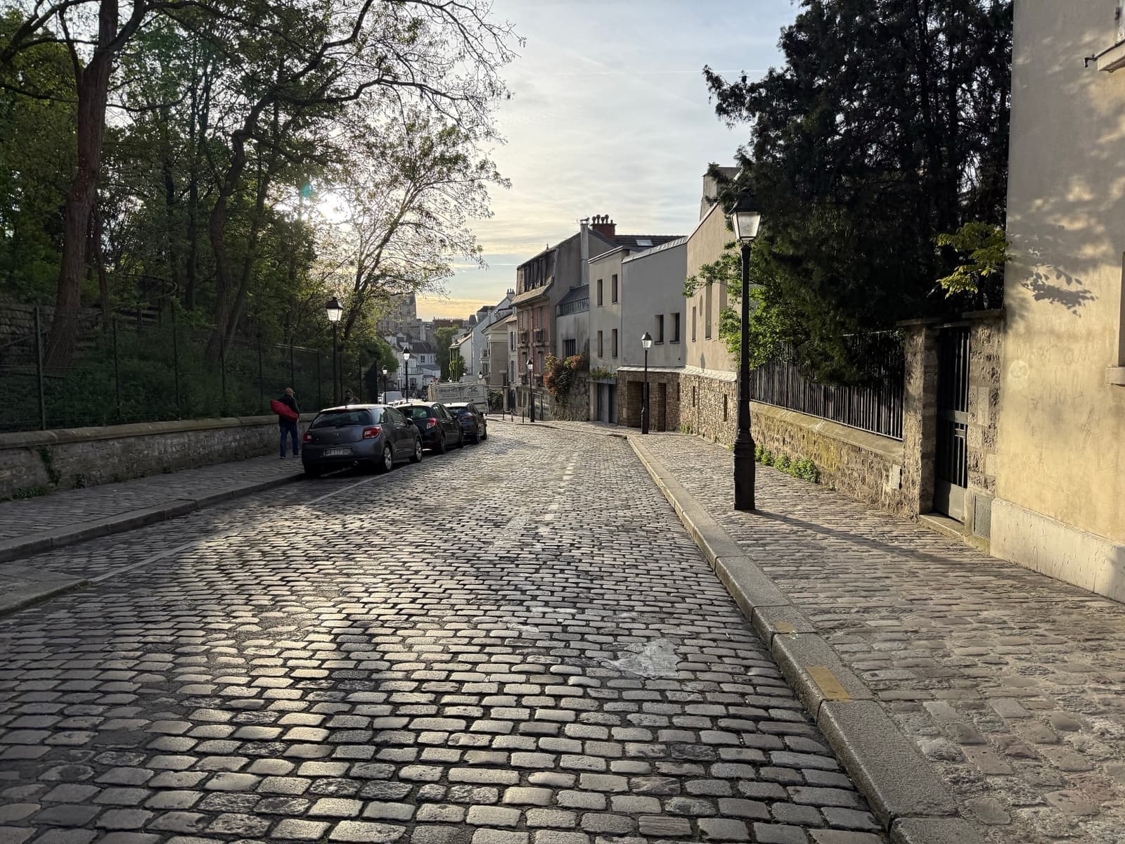 A narrow cobbled street curving between a stone wall and trees