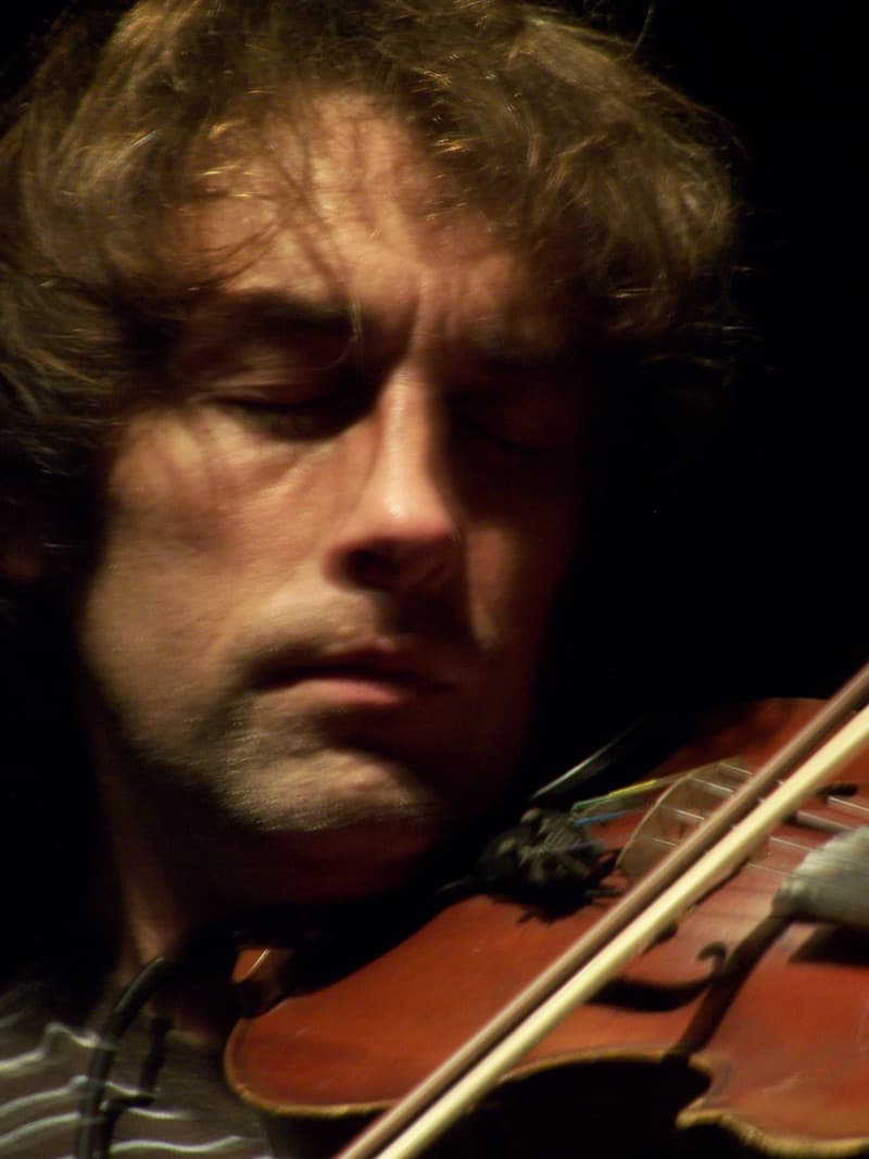 Yann Tiersen, eyes lowered, bowing a violin