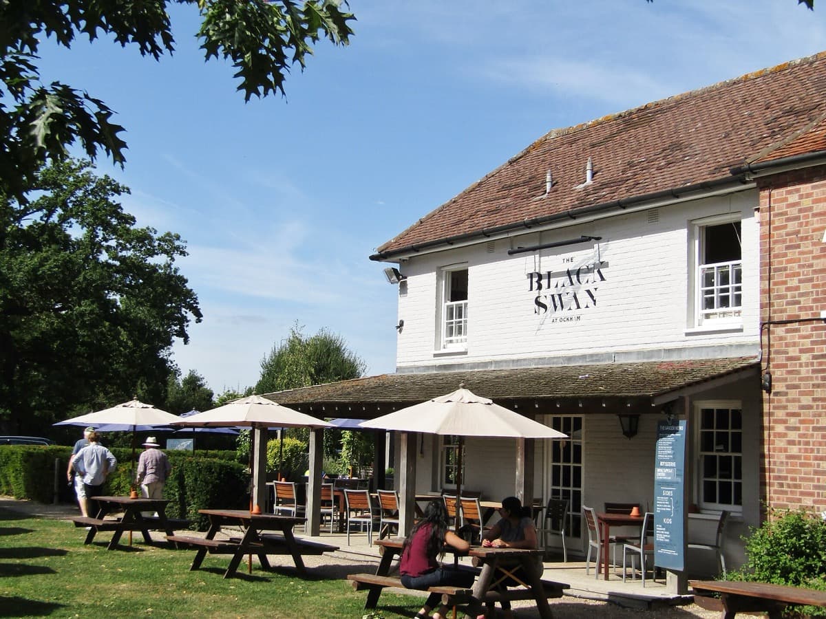 A white-fronted country pub with a hanging sign beside a lane