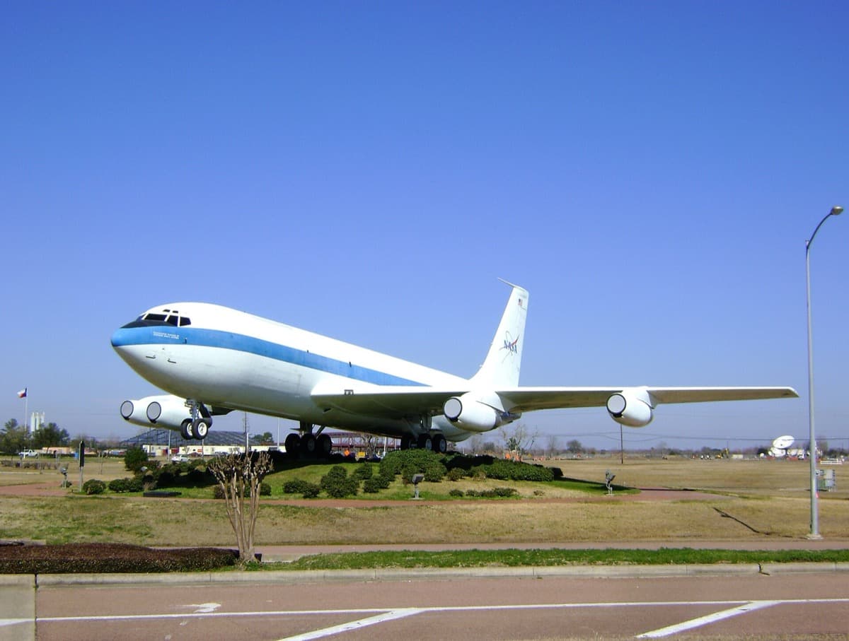 A white four-engined aircraft on an apron under a pale sky