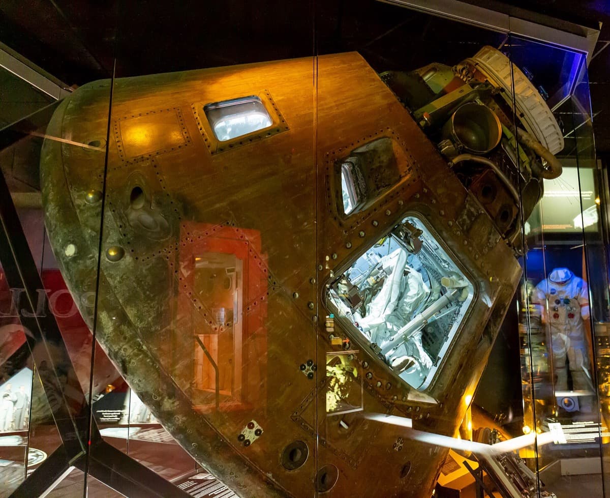A scorched conical spacecraft capsule displayed in a gallery