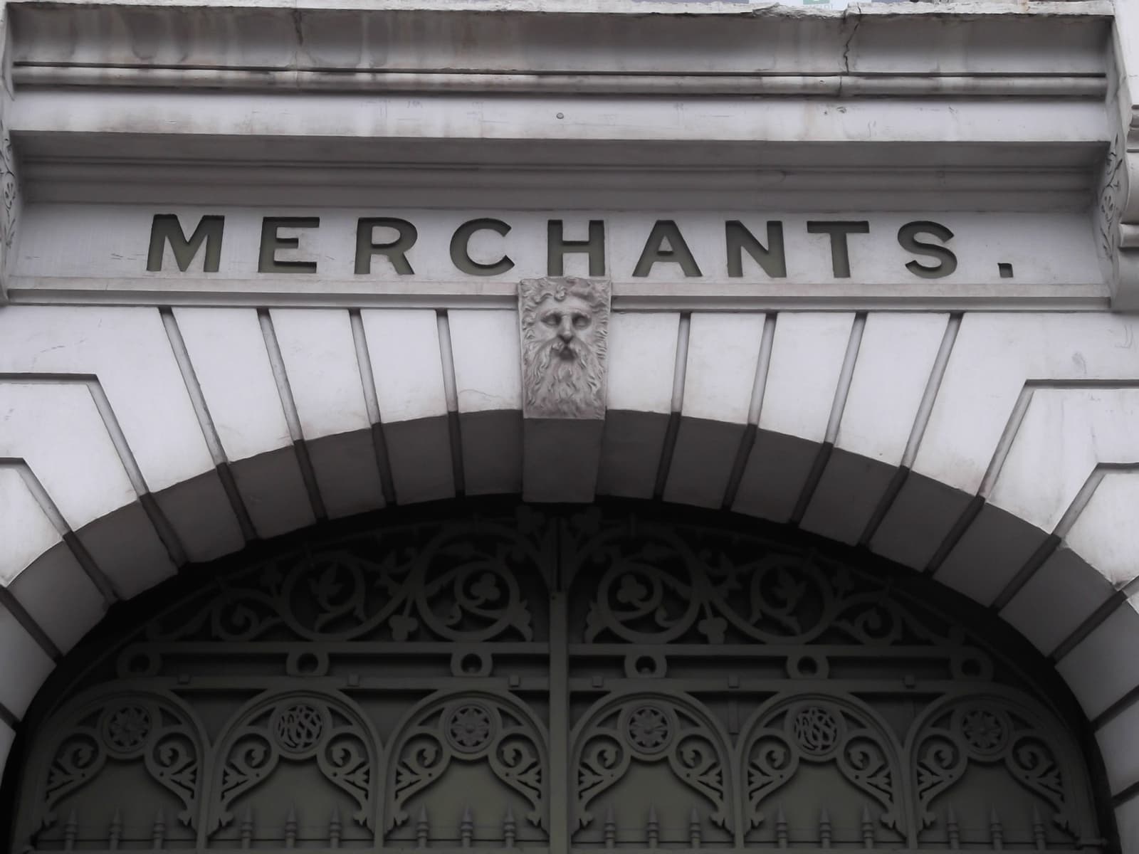 A carved stone arch over iron gates, with the word Merchants cut above