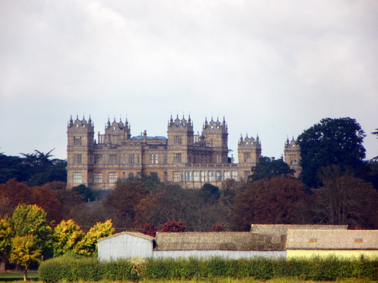 A towered Victorian mansion in honey-coloured stone rises above autumn trees