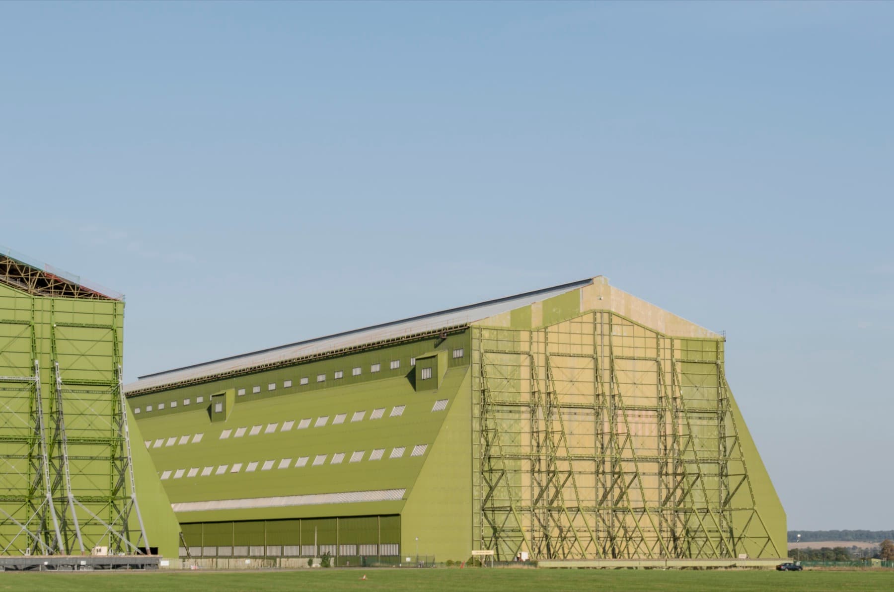 A vast green-clad airship hangar with buttressed sides stands on flat grass