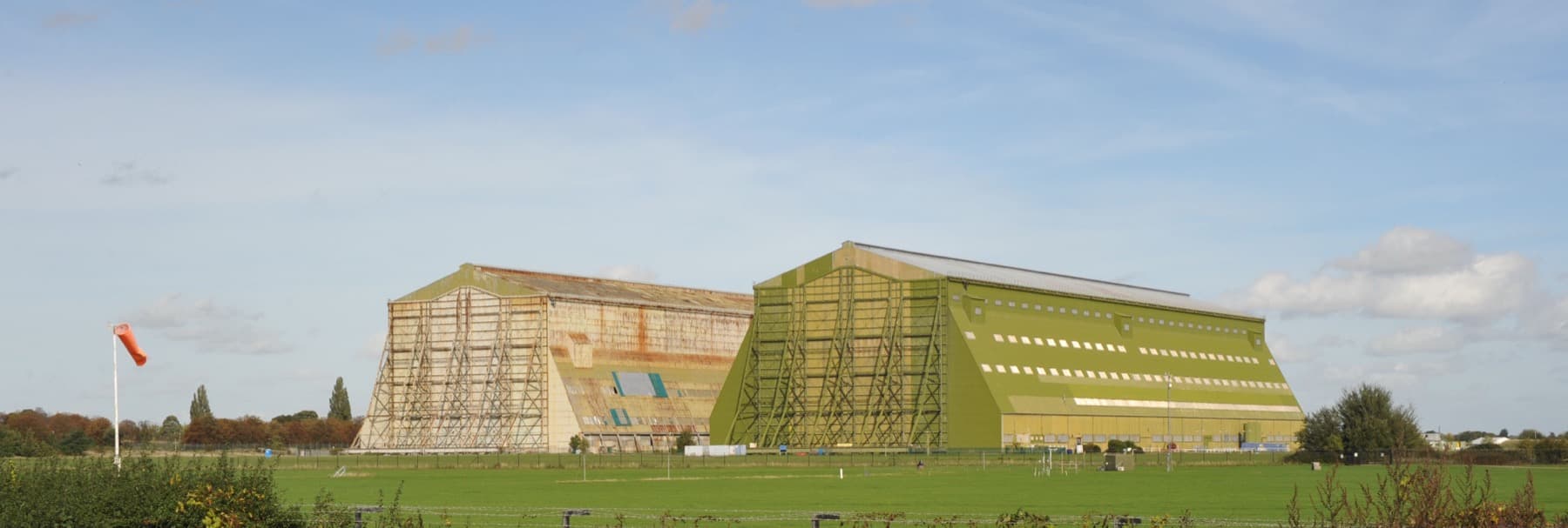Two enormous hangars, one pale and one green, rise from flat farmland