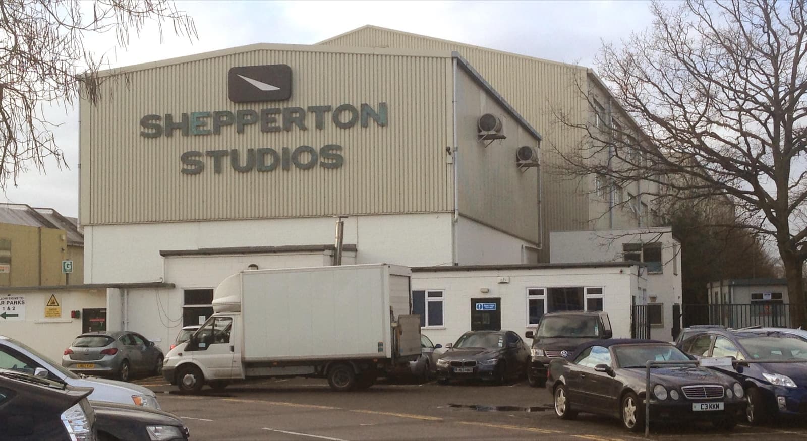 A pale studio building marked Shepperton Studios with parked cars in front