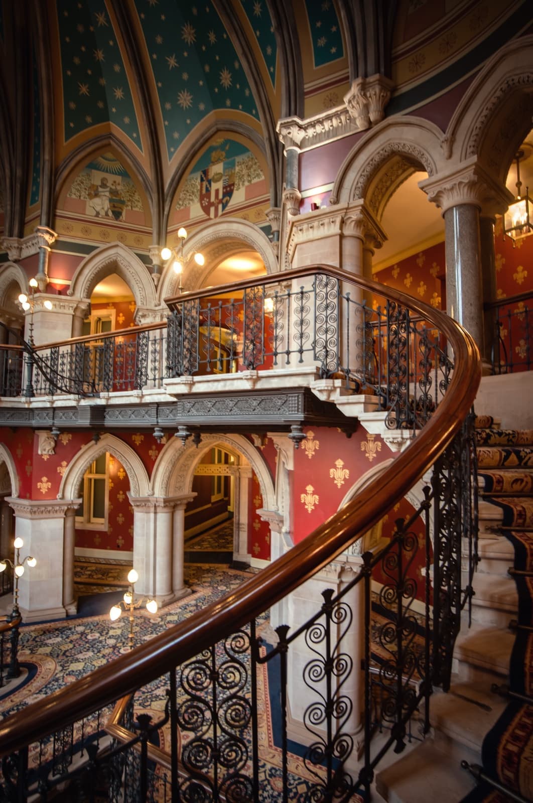 A Gothic stone staircase with wrought-iron balustrades curves under painted vaults