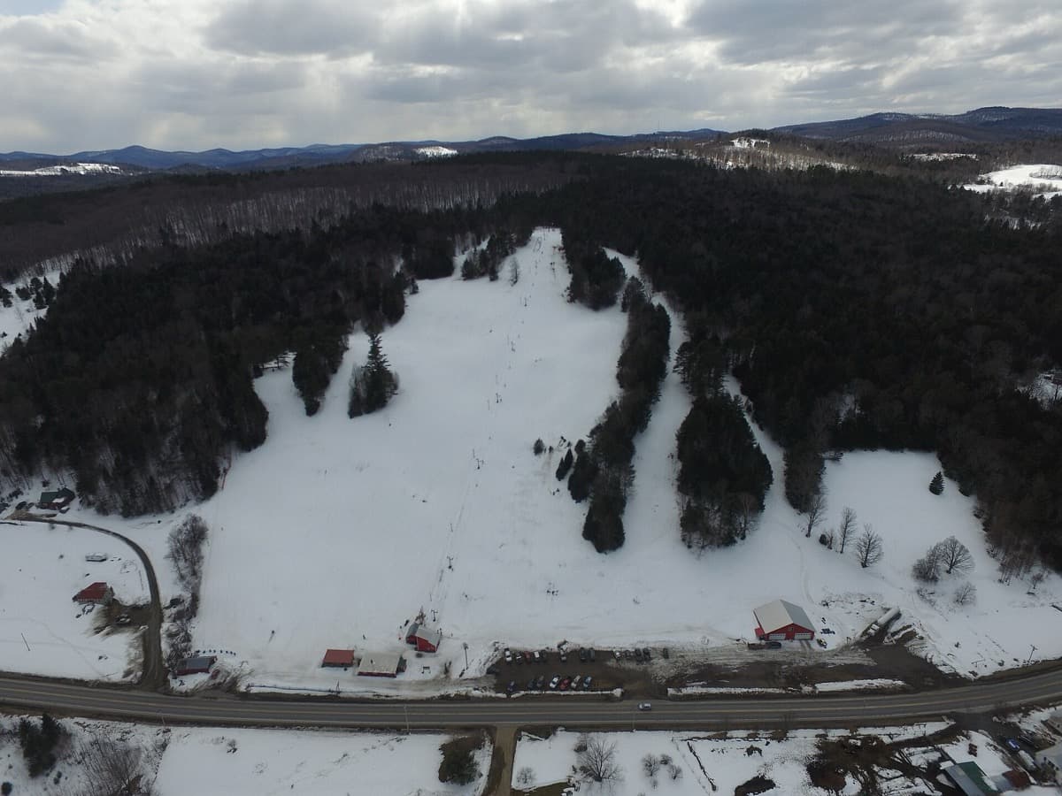 A snowy wooded hillside with a ski slope seen from the air