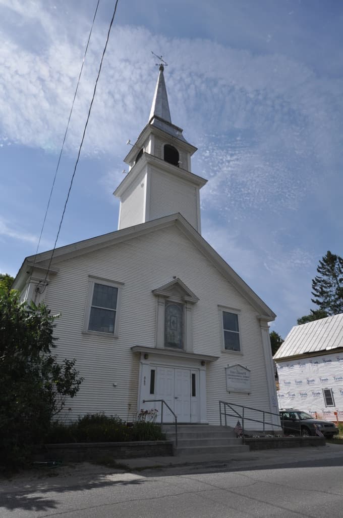 A white village church with a steeple under trees
